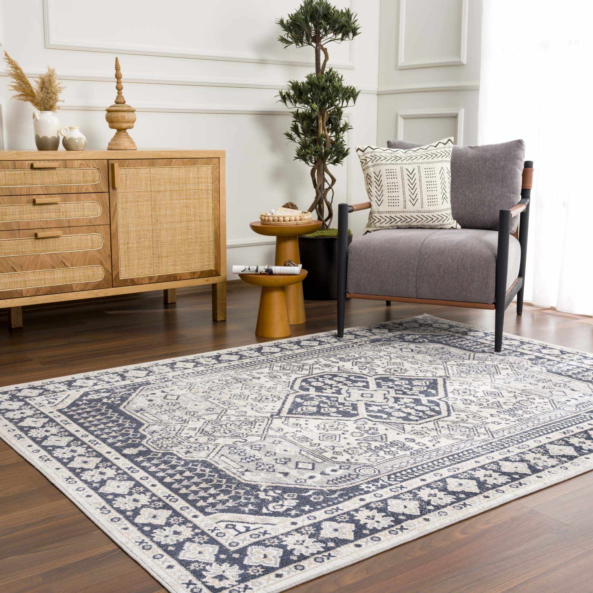 "Cabacungan washable rug in cream and gray placed in modern room with armchair and wood accents, enhancing cozy ambiance."