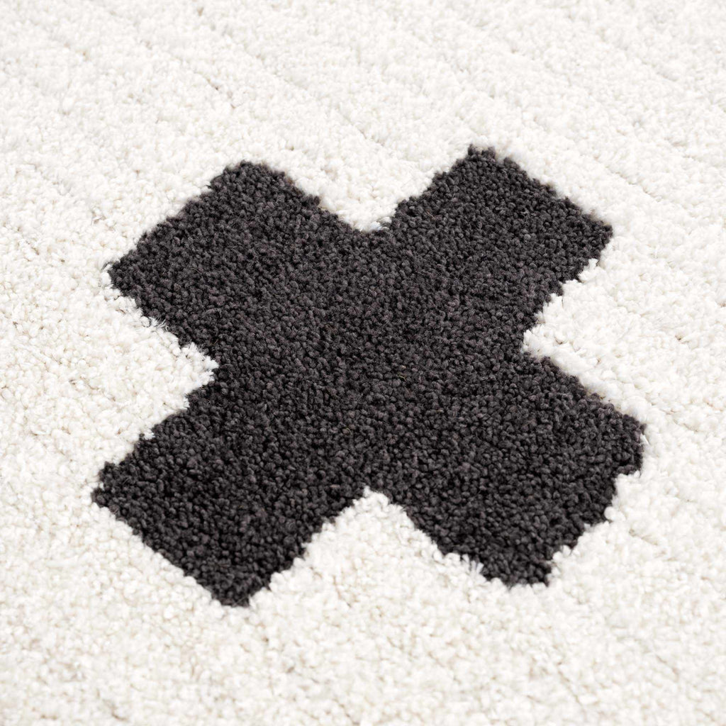 Macro shot of black cross on Erath Area Rug. High-pile polypropylene and polyester blend for comfort and resilience.