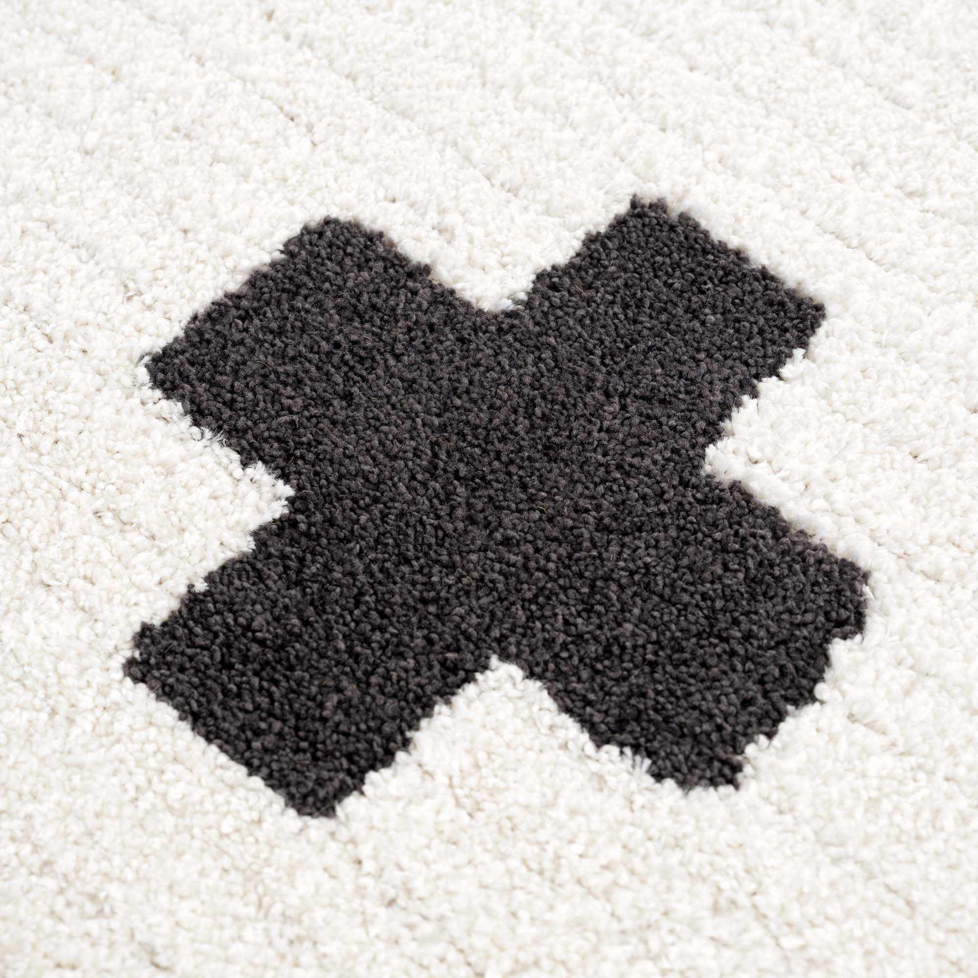 Macro shot of black cross on Erath Area Rug. High-pile polypropylene and polyester blend for comfort and resilience.