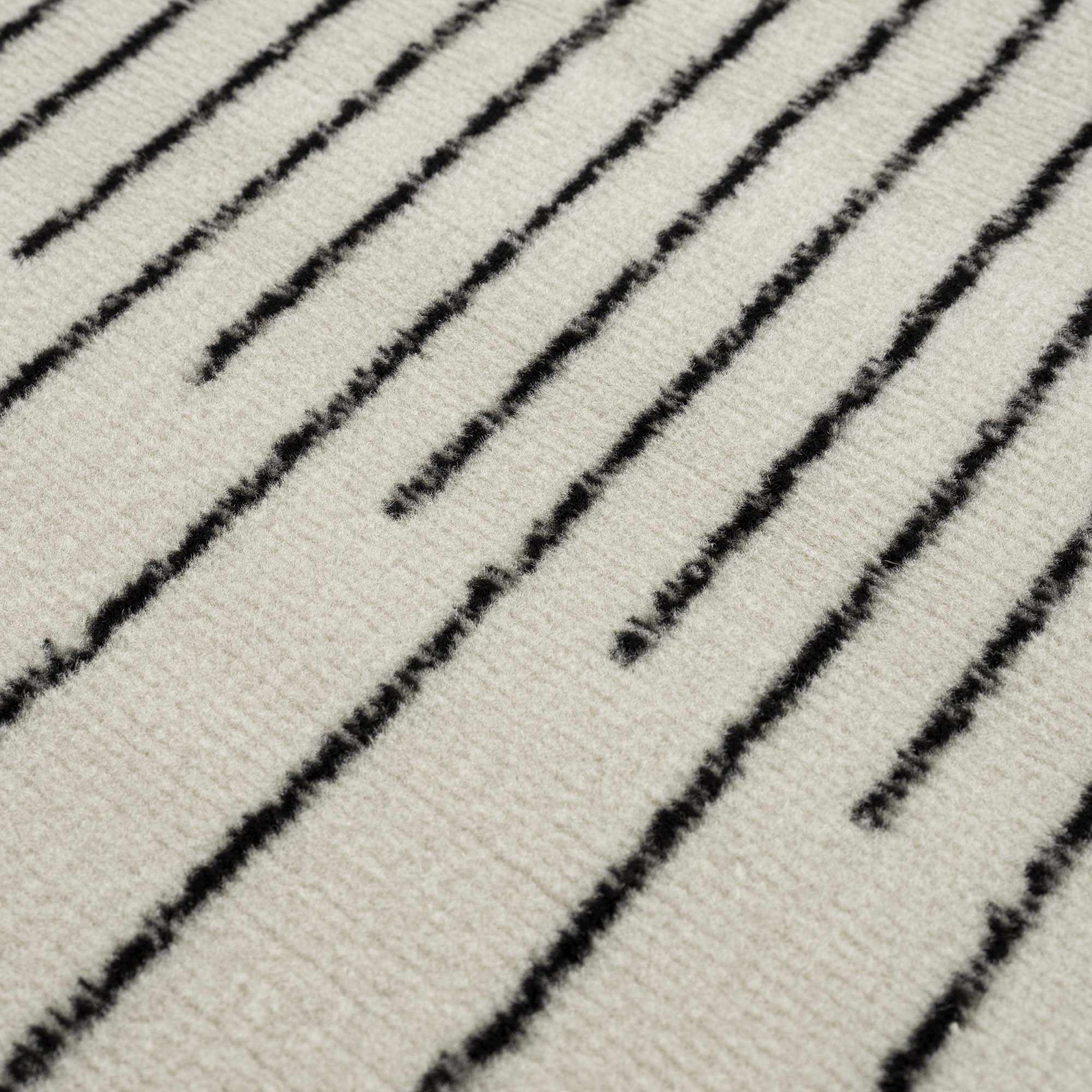 "Macro view of Angus Black White Rug surface with vertical black lines on white background, emphasizing texture."